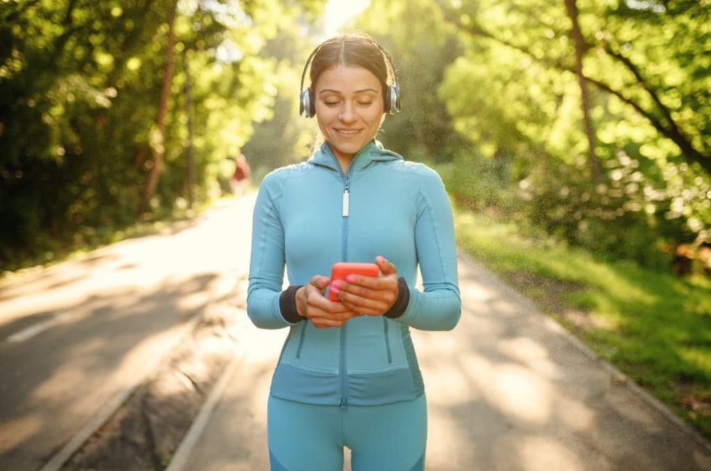 A woman using kratom happily training outdoors in a park while wearing headsets