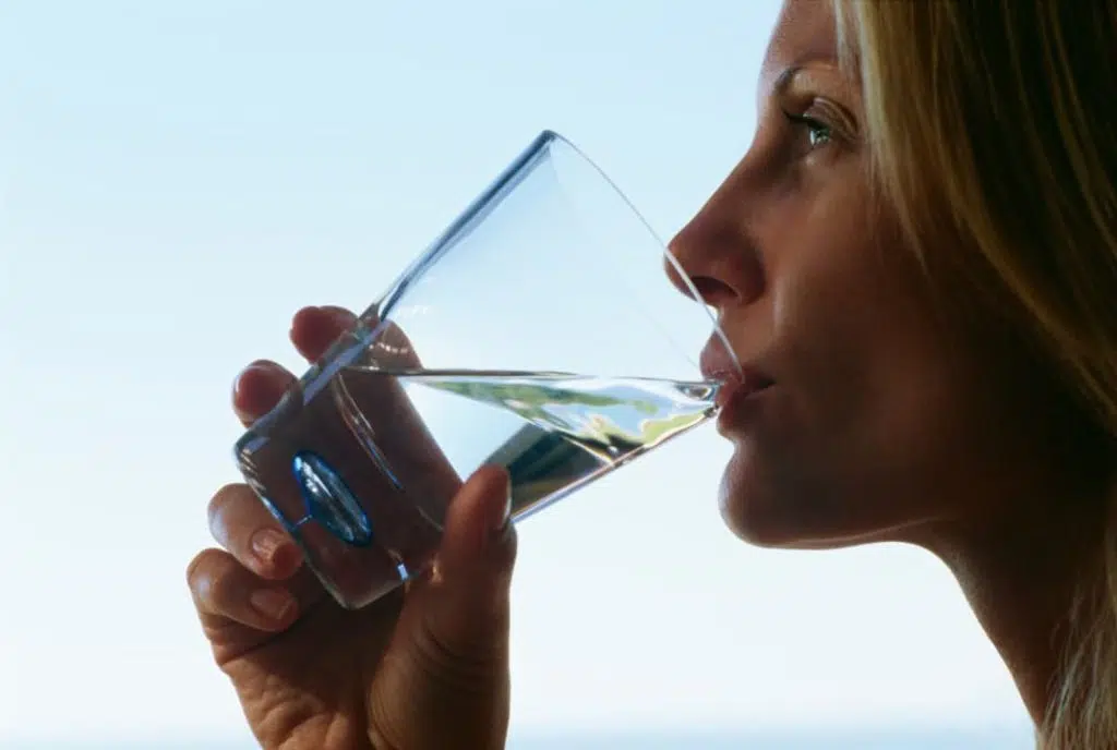 A woman drinking water from a glass of water while taking kratom