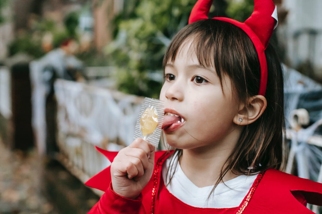 Child in a devil's costume licking a hard candy in wrapper